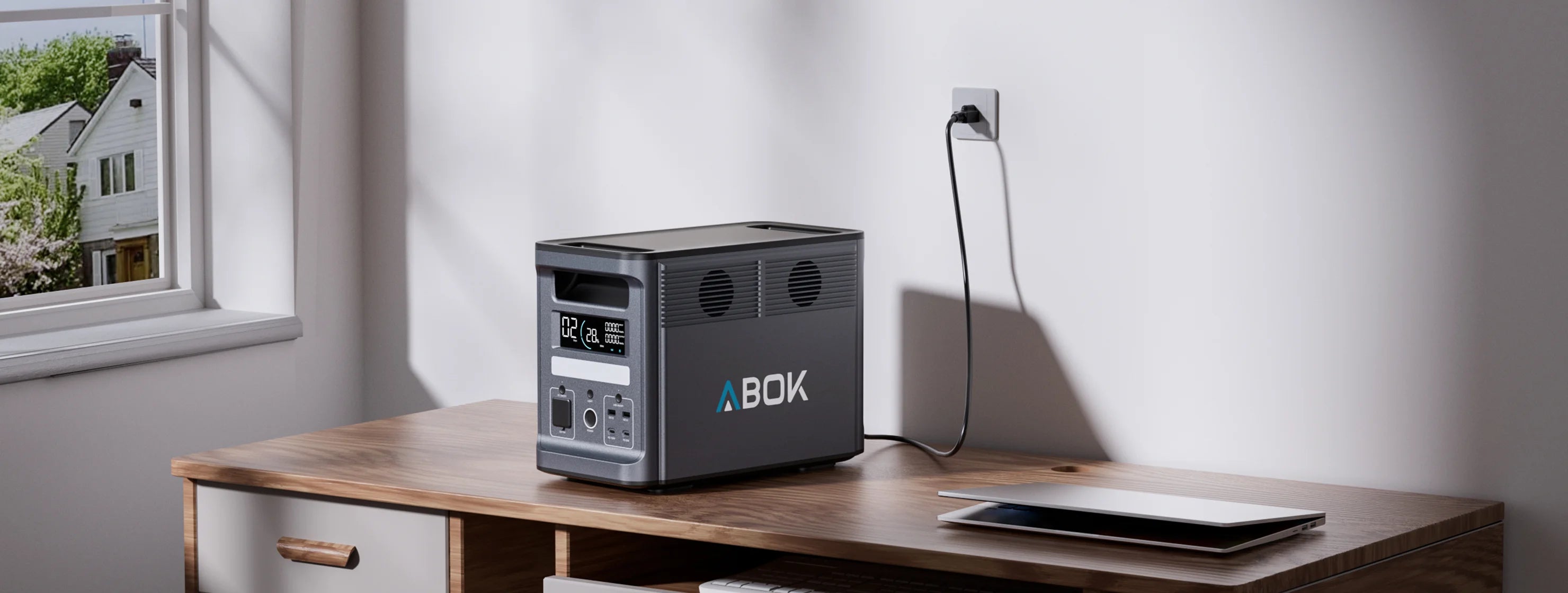 ABOK Ark2000 charging from a household wall outlet beside a laptop in a wide home office scene